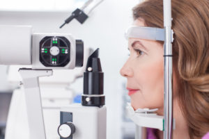 Middle aged woman is looking into eye test equipment with concentration. She is sitting in profile in oculist lab